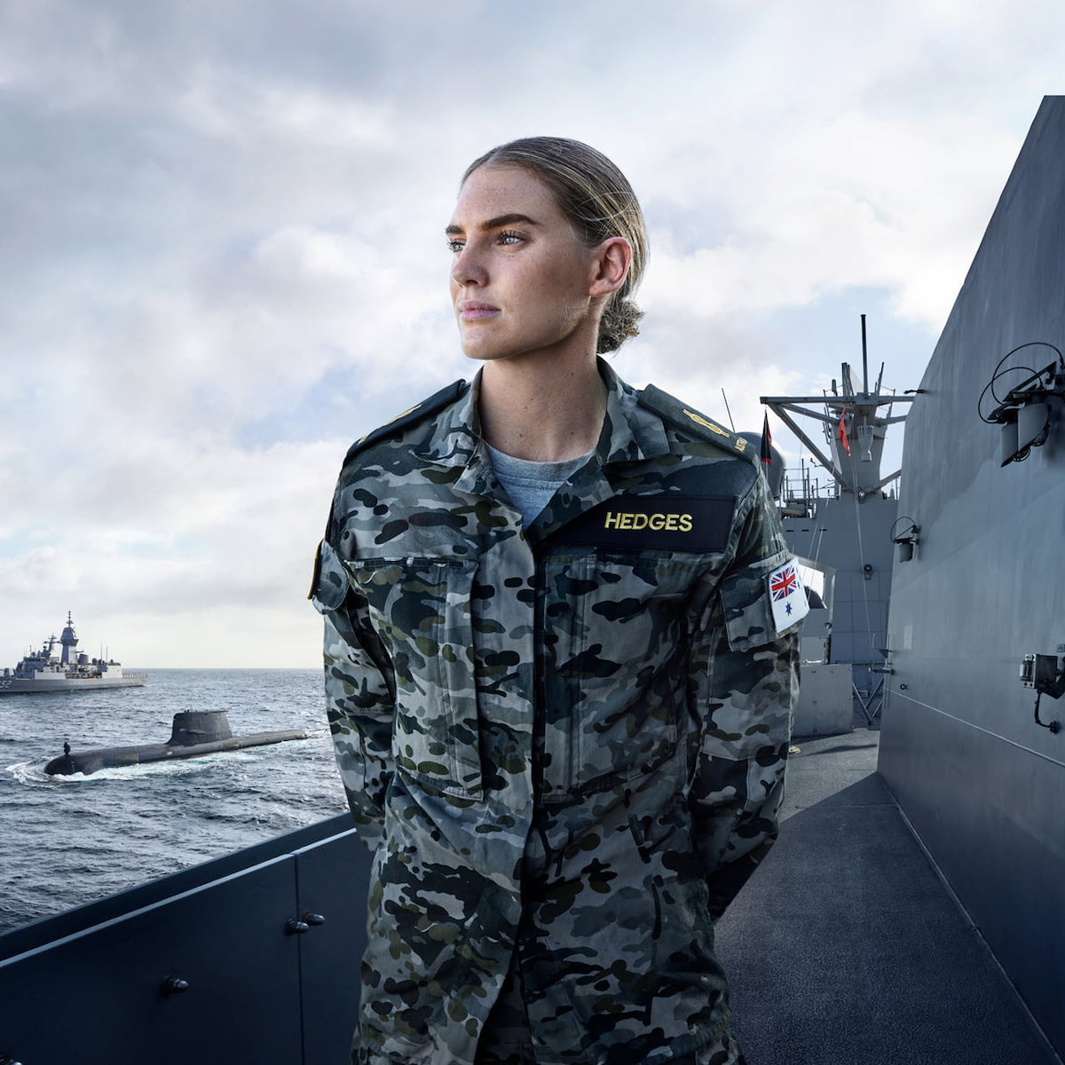 A woman in camouflage uniform stands on a ship, ready for action.