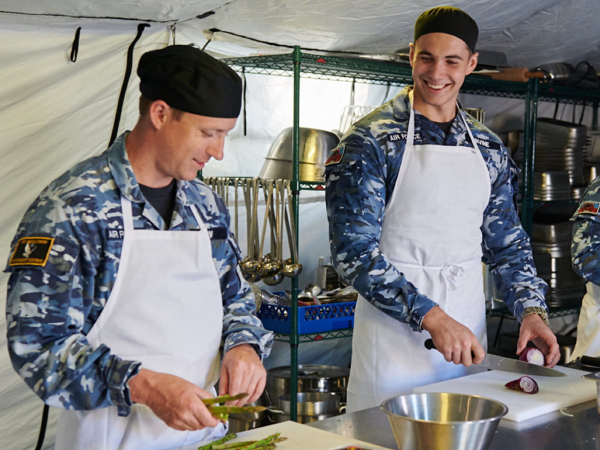 Two Air Force chefs chop food in the kitchen.