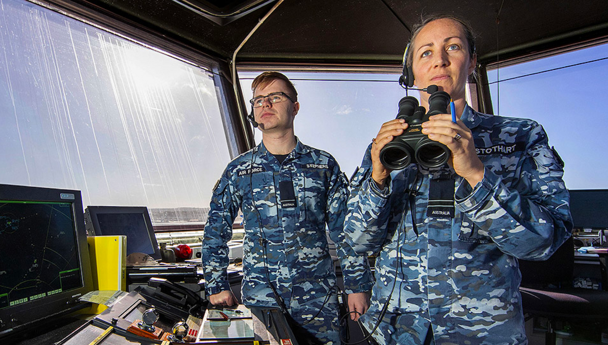 Two Air Force members standing in a control tower looking out. 