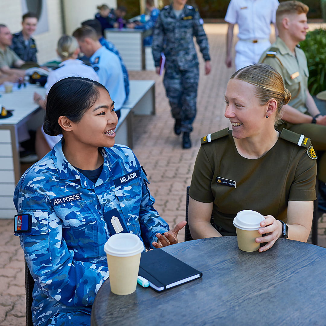 Two students in uniform are enjoying a coffee on campus.
