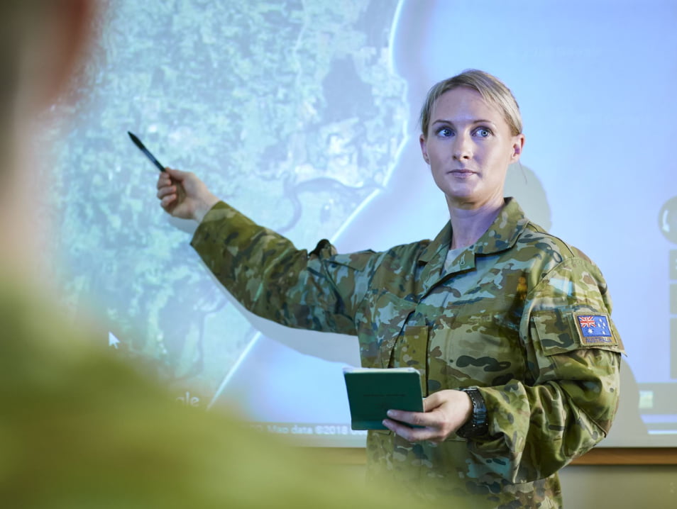 A woman in army uniform points at a whiteboard.